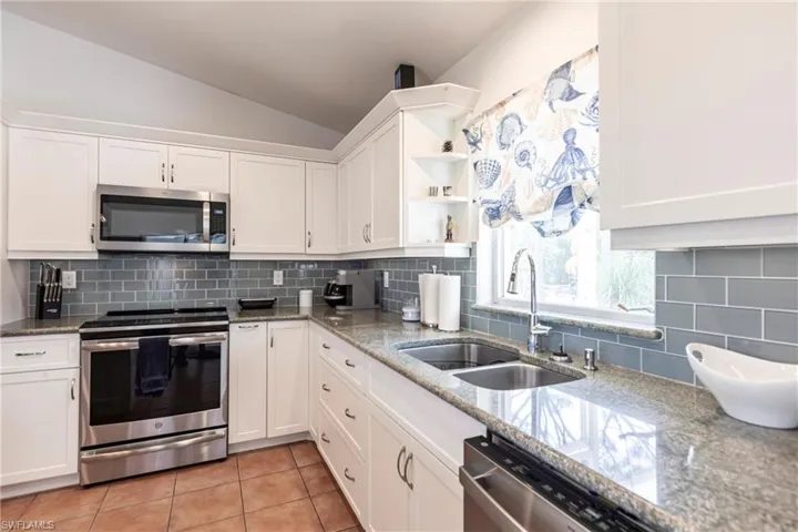Kitchen with stainless steel appliances, lofted ceiling, white cabinets, open shelves, and tasteful backsplash
