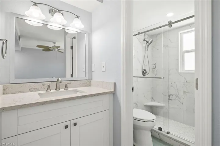 Guest bedroom full bath with toilet, a marble finish shower, ceiling fan, and quartz vanity