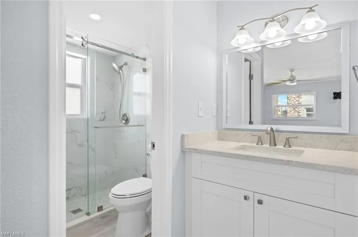 Primary bedroom full bathroom featuring a marble finish shower, toilet, quartz counter vanity, and a ceiling fan
