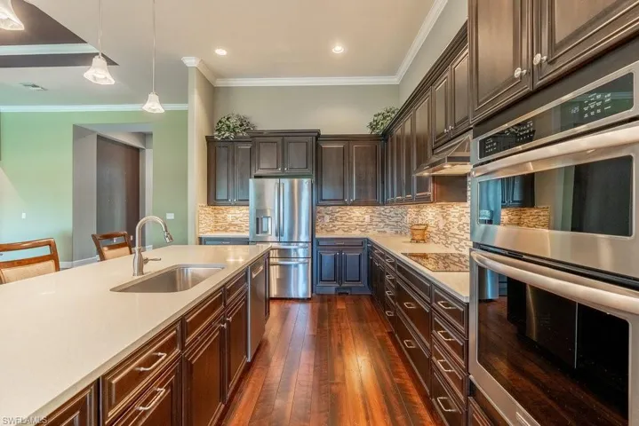 Kitchen with pendant lighting, sink, dark hardwood / wood-style floors, appliances with stainless steel finishes, and dark brown cabinets