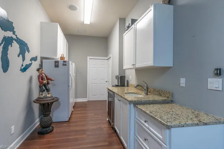 Kitchen with white cabinets, sink, dark hardwood / wood-style floors, light stone countertops, and white fridge