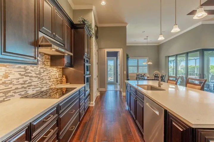 Kitchen with pendant lighting, sink, dark hardwood / wood-style floors, ornamental molding, and appliances with stainless steel finishes