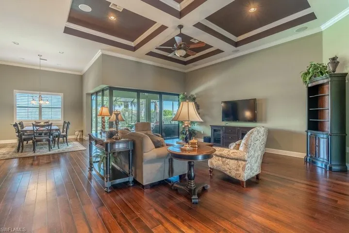 Living room with ceiling fan with notable chandelier, dark hardwood / wood-style flooring, ornamental molding, and coffered ceiling