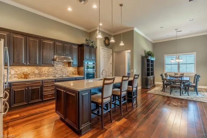 Kitchen featuring a center island with sink, dark hardwood / wood-style floors, a breakfast bar area, and hanging light fixtures