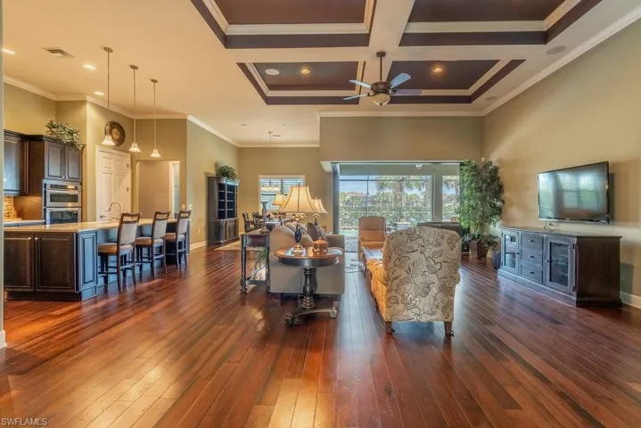Living room featuring ceiling fan, dark hardwood / wood-style flooring, crown molding, and coffered ceiling