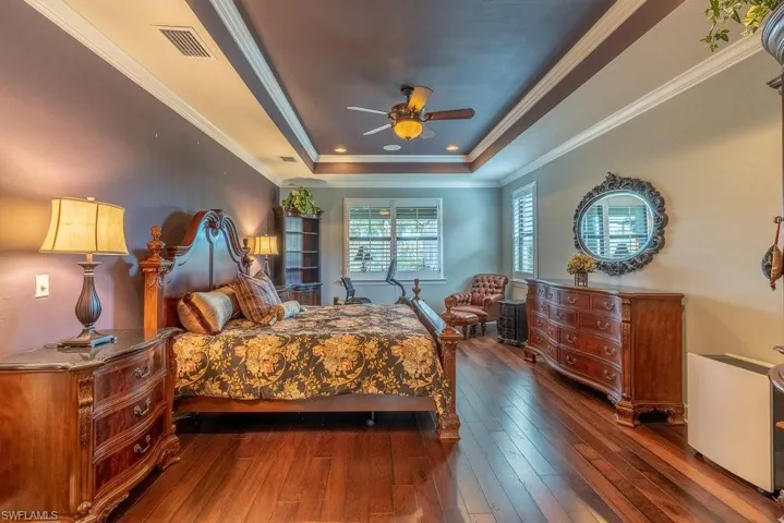 Bedroom featuring ceiling fan, a raised ceiling, ornamental molding, and dark wood-type flooring