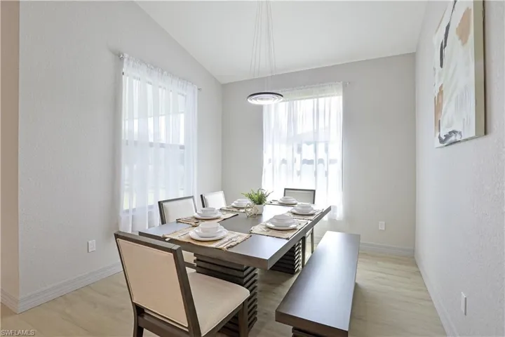 Dining space with a textured wall, light wood-style flooring, and vaulted ceiling