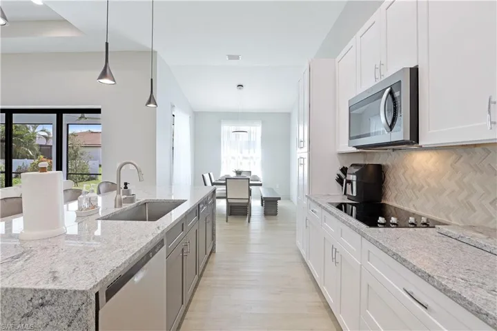 Kitchen featuring white cabinets, decorative light fixtures, light stone counters, stainless steel appliances, and decorative backsplash