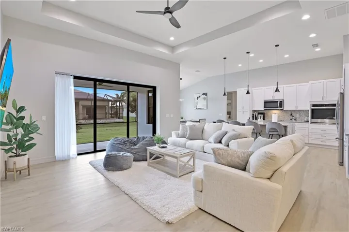 Living room featuring light wood-style flooring, a ceiling fan, a tray ceiling, recessed lighting, and a high ceiling