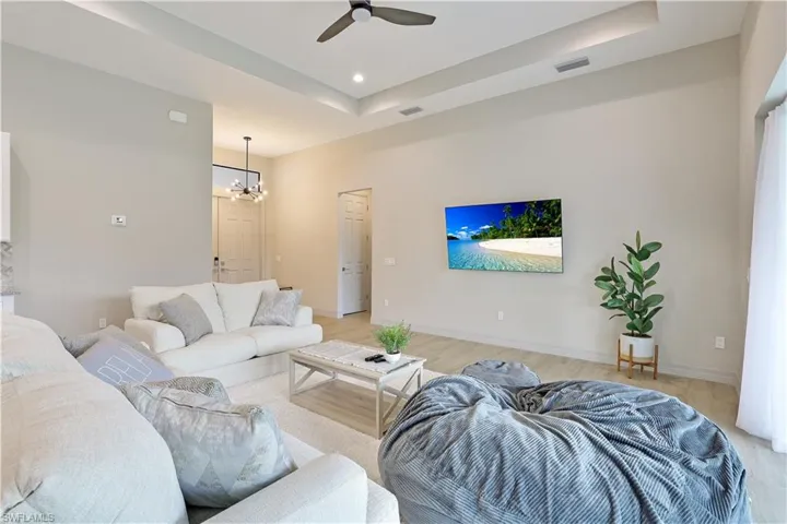 Living room with a chandelier, a tray ceiling, wood finished floors, ceiling fan, and recessed lighting