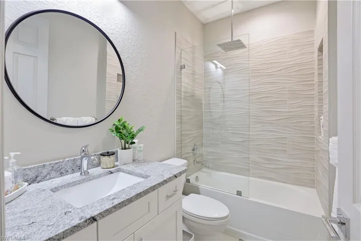 Bathroom featuring a textured wall, a combined bath / shower with rainfall shower, and vanity