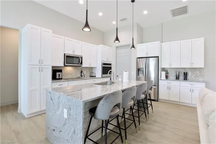 Kitchen with light stone countertops, decorative light fixtures, a kitchen breakfast bar, stainless steel appliances, and recessed lighting