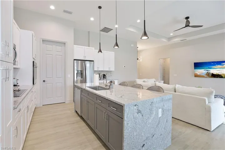 Kitchen with gray cabinets, white cabinetry, decorative light fixtures, an island with sink, and backsplash