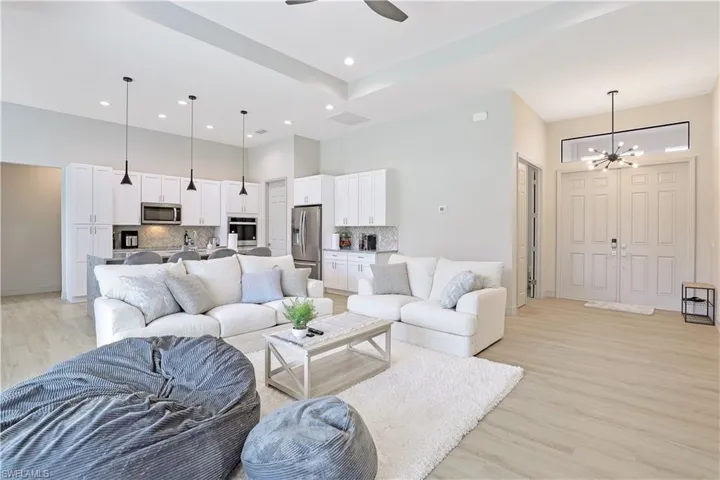 Living area with light wood finished floors, a chandelier, a ceiling fan, a towering ceiling, and recessed lighting