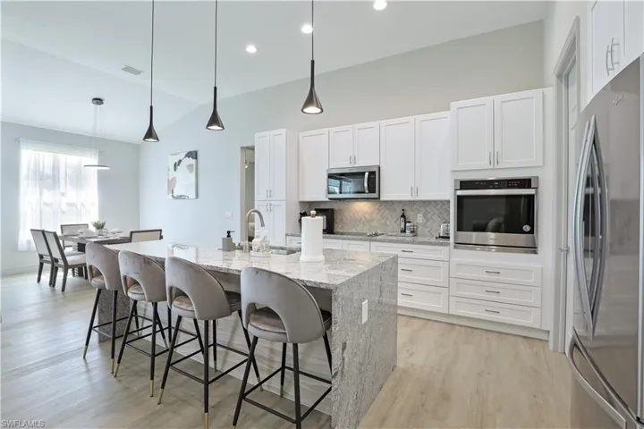 Kitchen with decorative light fixtures, light stone countertops, tasteful backsplash, white cabinets, and a center island with sink