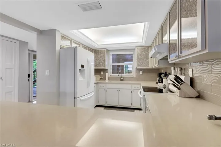 Kitchen featuring white appliances, under cabinet range hood, tasteful backsplash, and light countertops