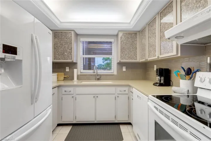 Kitchen with white appliances, extractor fan, light tile patterned floors, tasteful backsplash, and light countertops