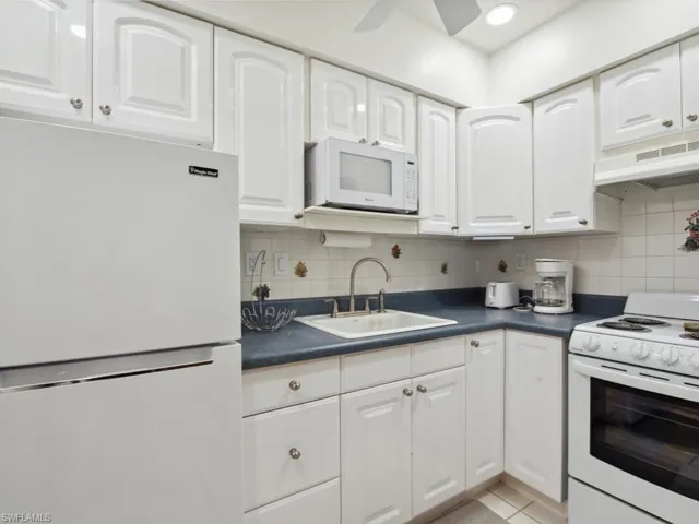 Kitchen with sink, white appliances, ceiling fan, white cabinetry, and decorative backsplash