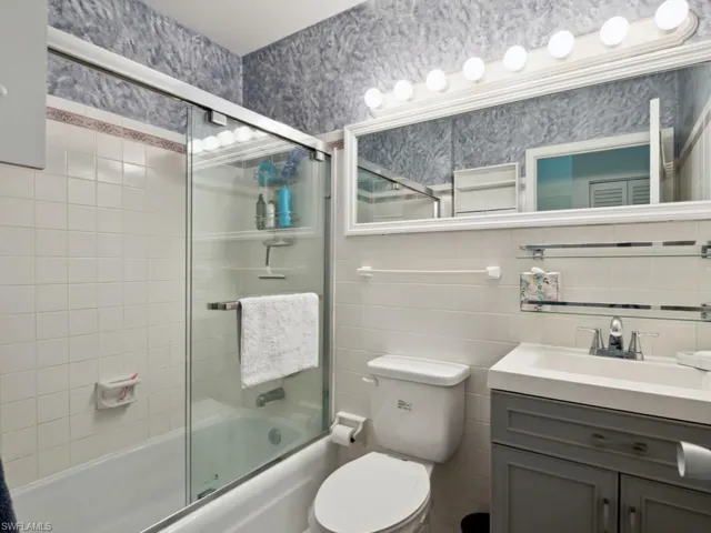 Full bathroom with shower / bath combination with glass door, tile walls, vanity, decorative backsplash, and toilet