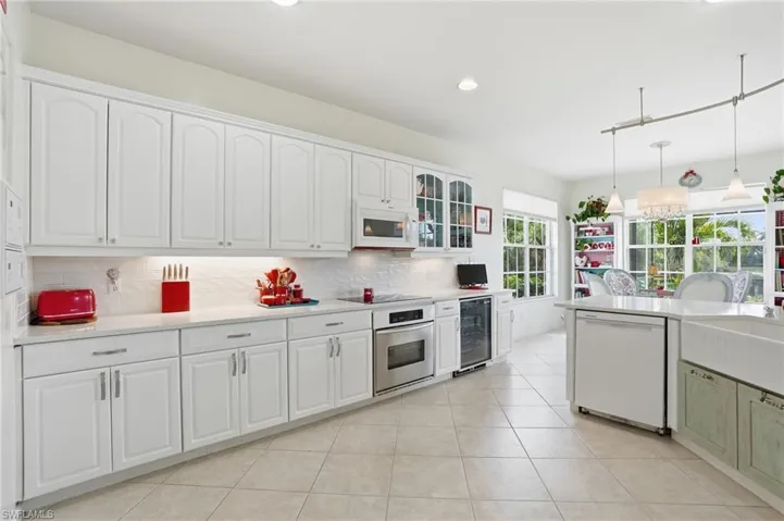 Kitchen with white appliances, glass fronted cabinets, decorative light fixtures, and white cabinetry