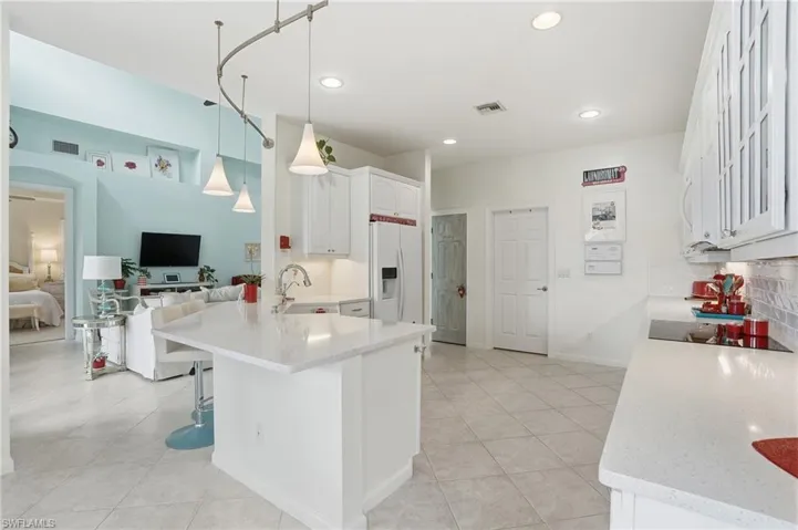 Kitchen featuring tasteful backsplash, white appliances, a peninsula, hanging light fixtures, and white cabinets