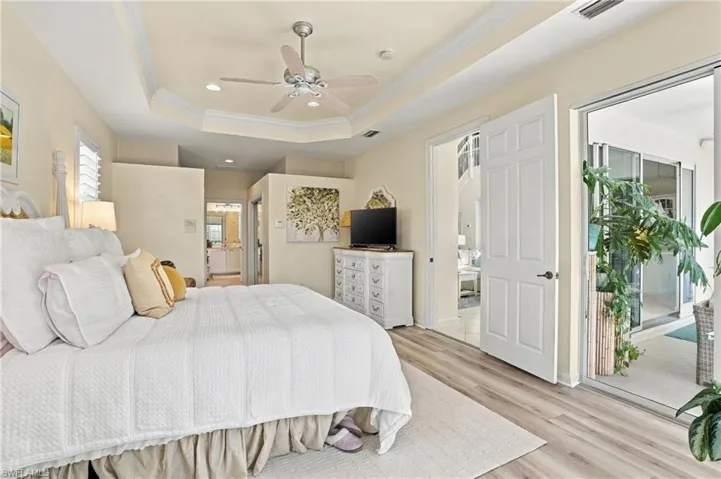 Tray ceiling with a central brushed-nickel ceiling fan, wood-finish flooring, and large sliding glass doors providing outdoor access
