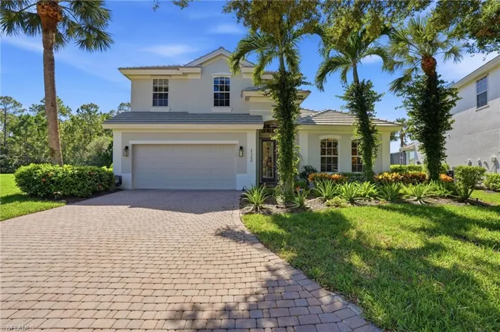 Two-story residence featuring a stucco facade, tiled roof, arched window detailing, and a paver driveway