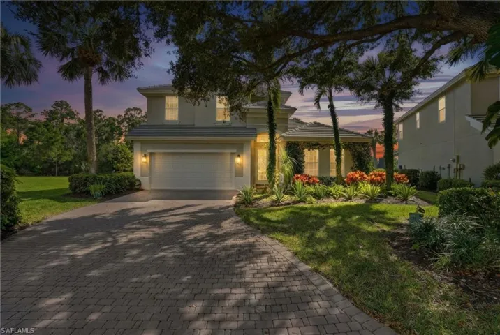View of front facade featuring decorative driveway, a garage, a lawn, stucco siding, and a tile roof