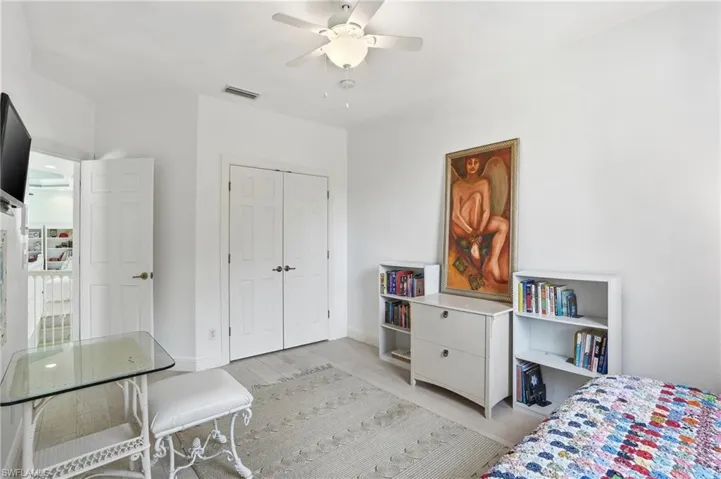 Neutral-toned interior featuring high ceilings, wood-finish flooring, a ceiling fan with integrated lighting, and double-door closet storage
