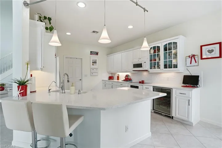 Kitchen featuring white cabinetry, solid-surface countertops, glass-front upper cabinet doors, under-cabinet lighting, and an integrated wine refrigerator