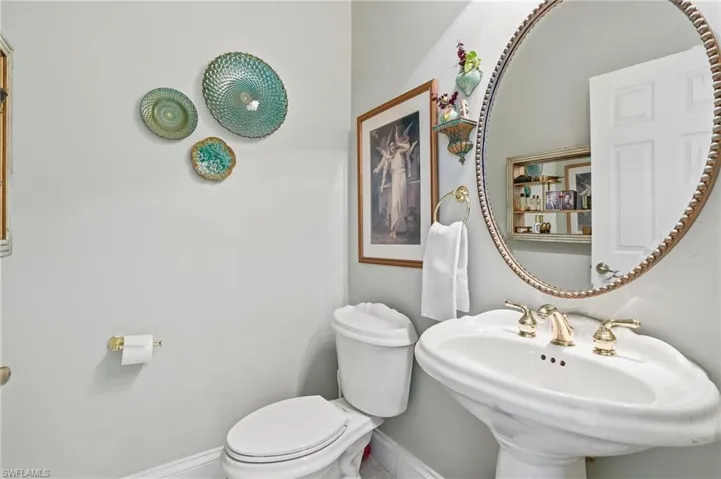 Powder room featuring a pedestal sink with a metallic widespread faucet, an oval mirror with a beaded frame, and a wall-mounted toilet