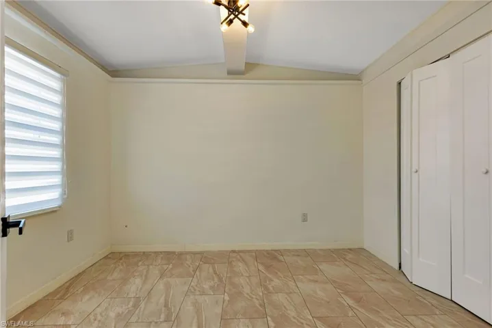 Unfurnished bedroom with lofted ceiling with beams and light tile flooring
