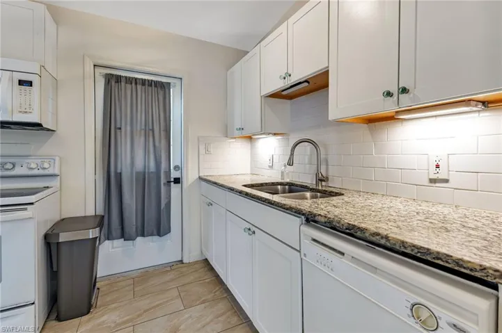 Kitchen featuring tasteful backsplash, white cabinetry, light stone countertops, sink, and white appliances