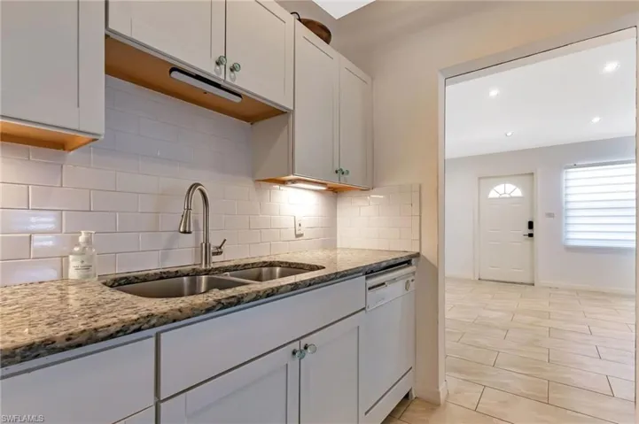 Kitchen with backsplash, sink, dishwasher, and stone counters