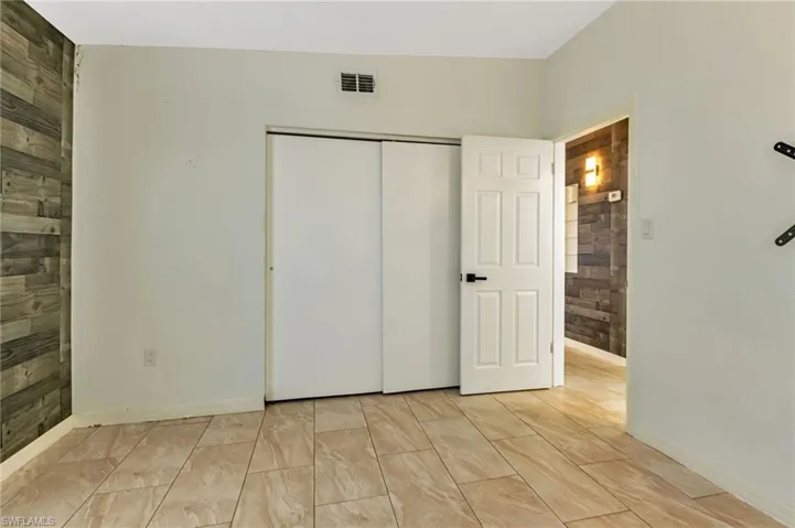 Unfurnished bedroom with wood walls, a closet, and light tile floors