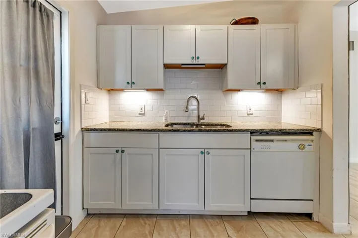 Kitchen with tasteful backsplash, dishwasher, vaulted ceiling, light stone counters, and sink
