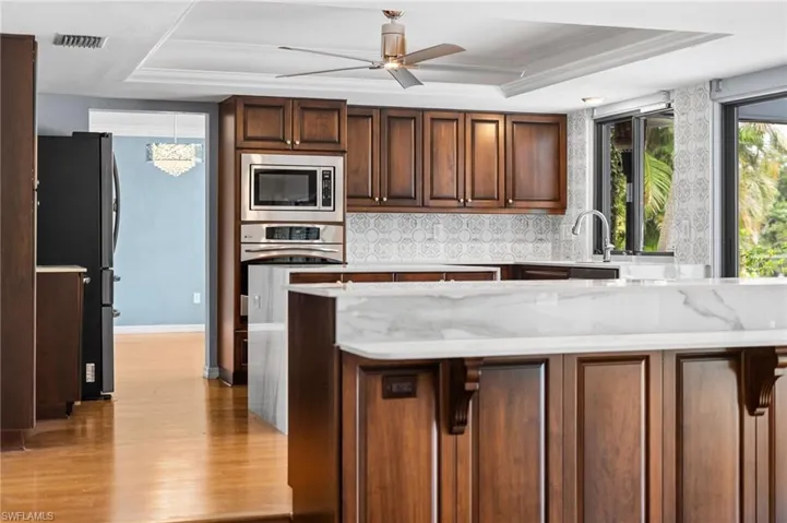 Kitchen with appliances with stainless steel finishes, light wood-style floors, a raised ceiling, a peninsula, and ceiling fan