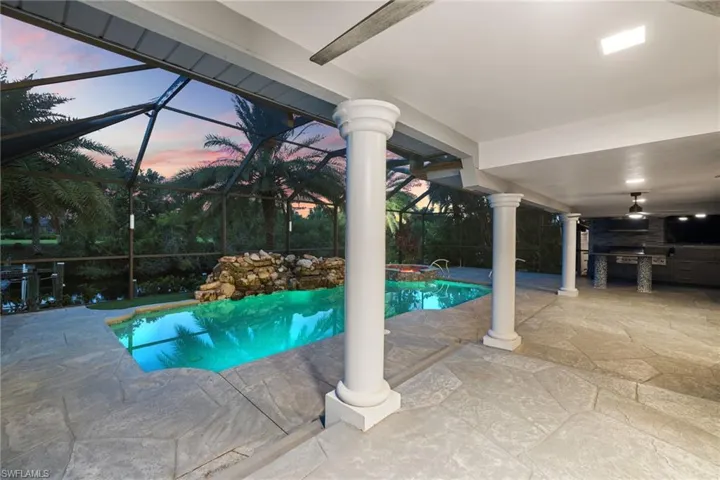 Pool at dusk with a patio area, glass enclosure, an outdoor kitchen, and a pool with connected hot tub