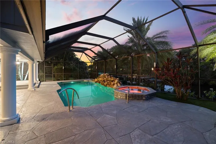 Pool at dusk featuring glass enclosure, a patio, and a pool with connected hot tub