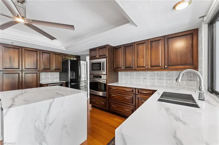 Kitchen with stainless steel appliances, a raised ceiling, ceiling fan, tasteful backsplash, and light wood-type flooring