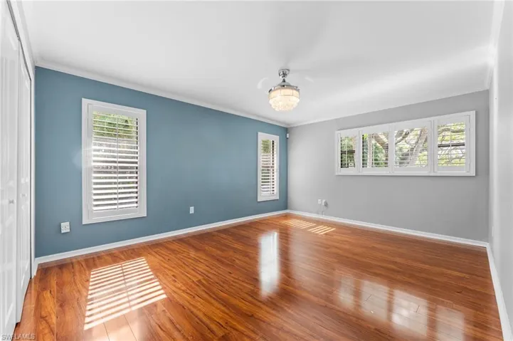 Empty room with ornamental molding, wood finished floors, and a chandelier