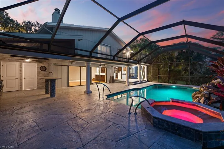 Pool at dusk featuring a patio area, a pool with connected hot tub, and glass enclosure