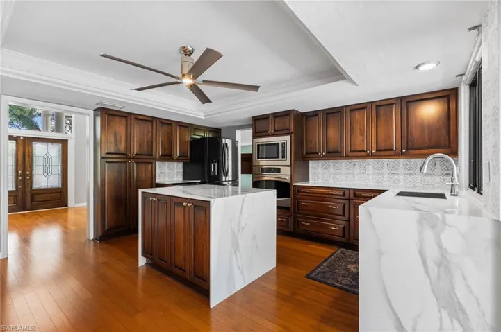 Kitchen with stainless steel appliances, a raised ceiling, a ceiling fan, a kitchen island, and backsplash