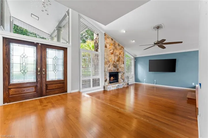 Foyer entrance with hardwood / wood-style flooring, ceiling fan, a stone fireplace, french doors, and crown molding