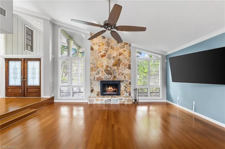 Unfurnished living room with vaulted ceiling, ornamental molding, wood finished floors, a fireplace, and ceiling fan