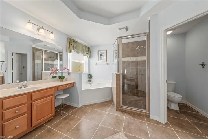 Primary bathroom featuring tile patterned flooring, a shower, soaking tub, toilet closet, and a vanity