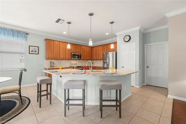 Kitchen with stainless steel appliances, light tile patterned floors, tiled backsplash, crown molding, and a kitchen breakfast bar