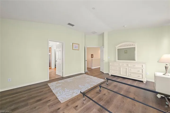 Primary bedroom featuring vaulted ceiling, laminate floors, and baseboards