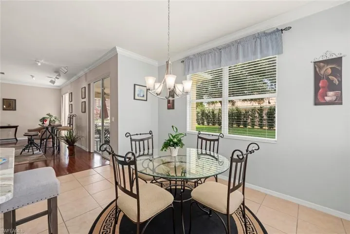 Dining space off family room featuring light tile patterned floors, a chandelier, crown molding, and windows