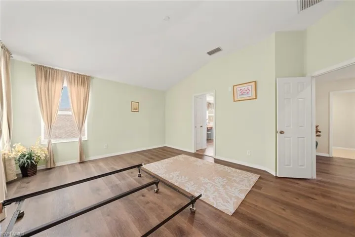 Primary bedroom featuring laminate flooring, vaulted ceilings, and multiple ceilings